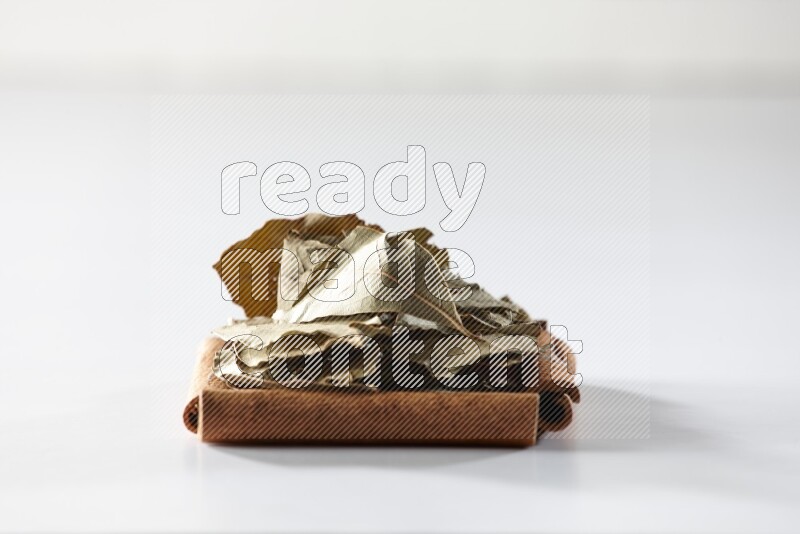 أربعة من أعواد القرفة مكونة شكل مربع بداخلها أوراق الغار علي خلفية بيضاء