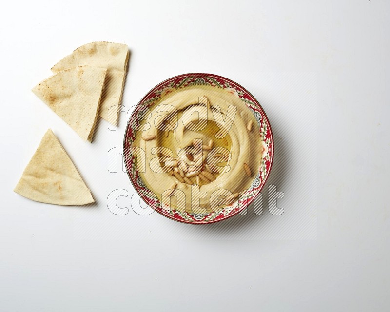 Hummus in a red plate with patterns garnished with pine nuts on a white background