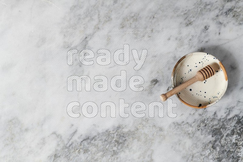 Multicolored Pottery bowl with wooden honey handle in it, on grey marble flooring, Top View