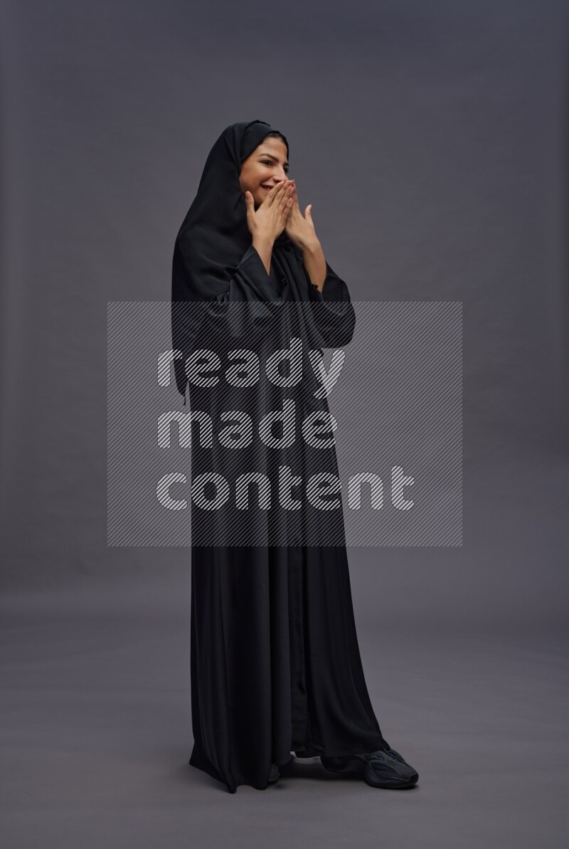 Saudi woman wearing Abaya standing hands behind head on gray background
