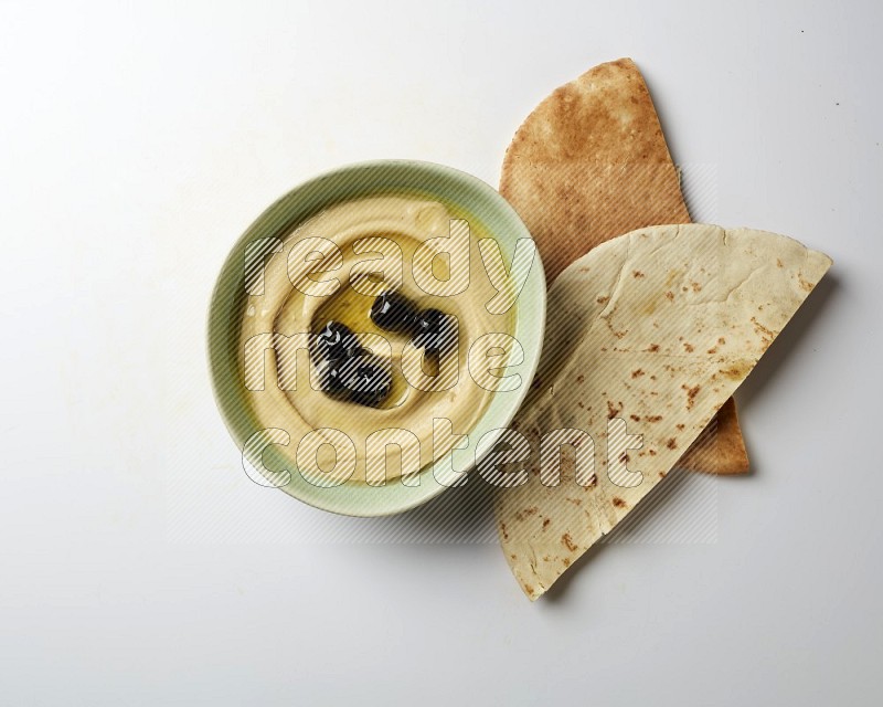 Hummus in a green plate garnished with black olives on a white background