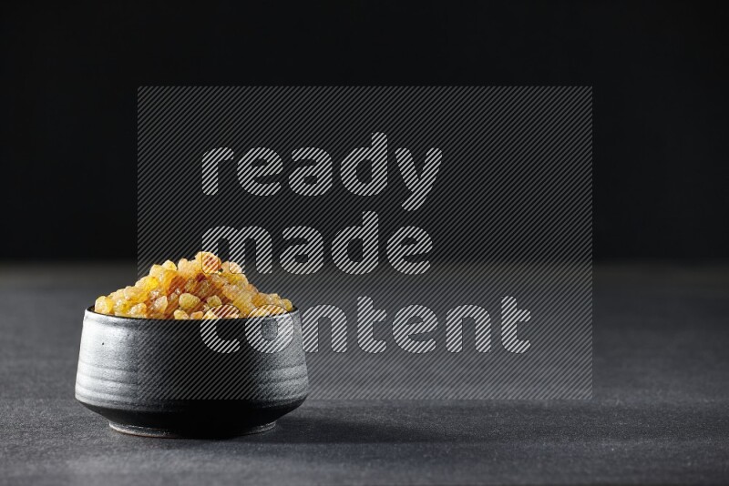 A black pottery bowl full of raisins on a black background in different angles