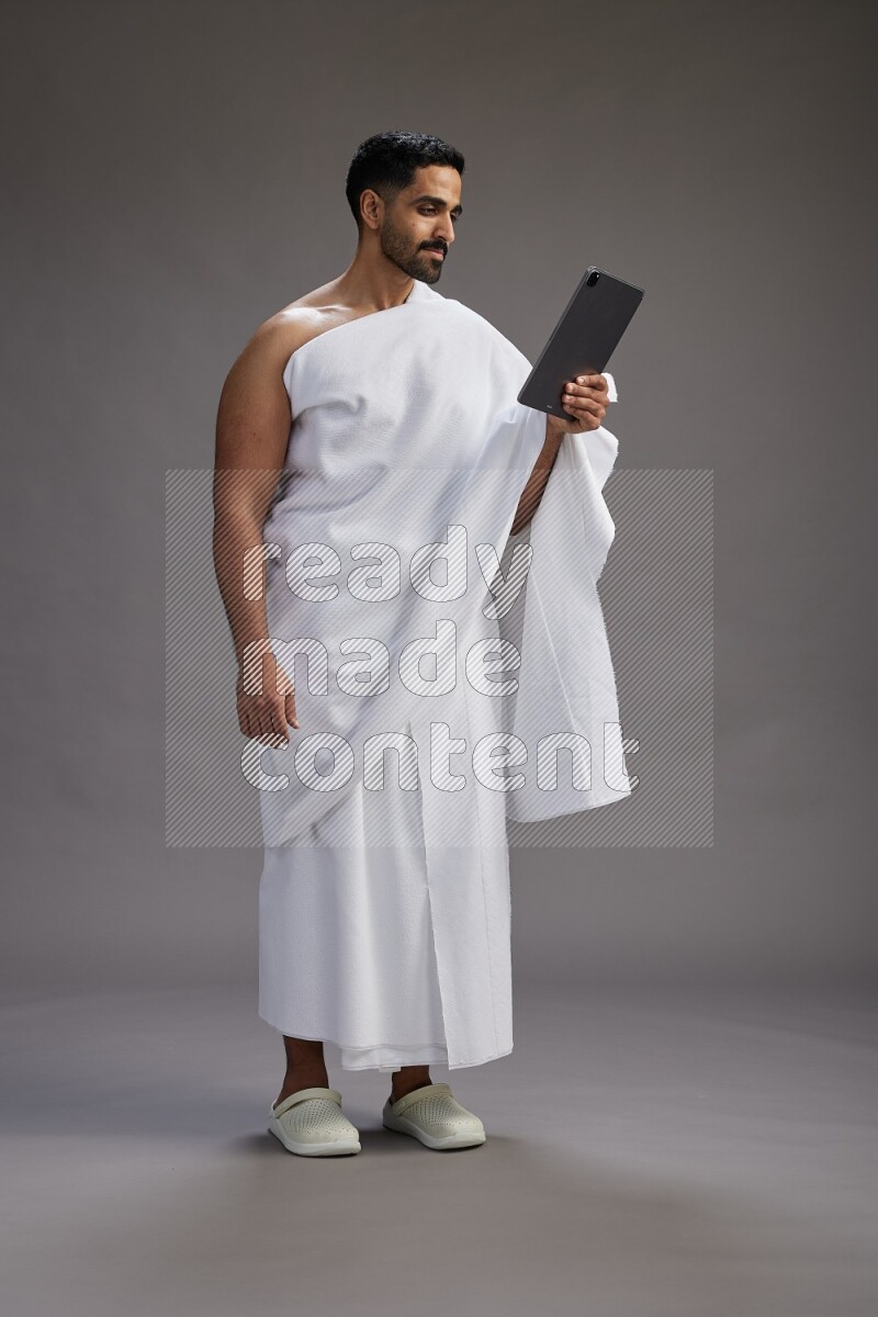 A man wearing Ehram and holding a tablet on gray background