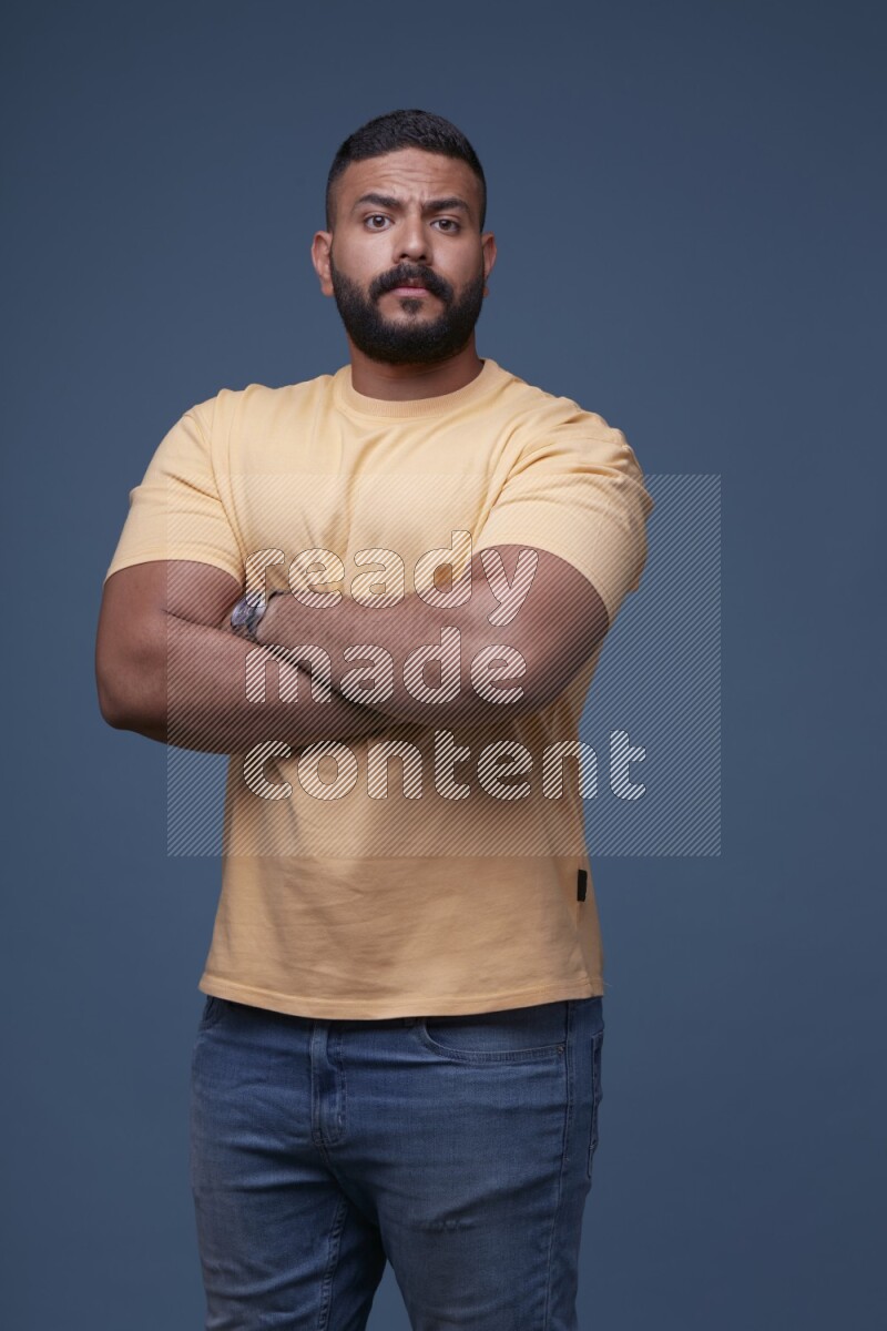A man posing in a blue background wearing a yellow shirt