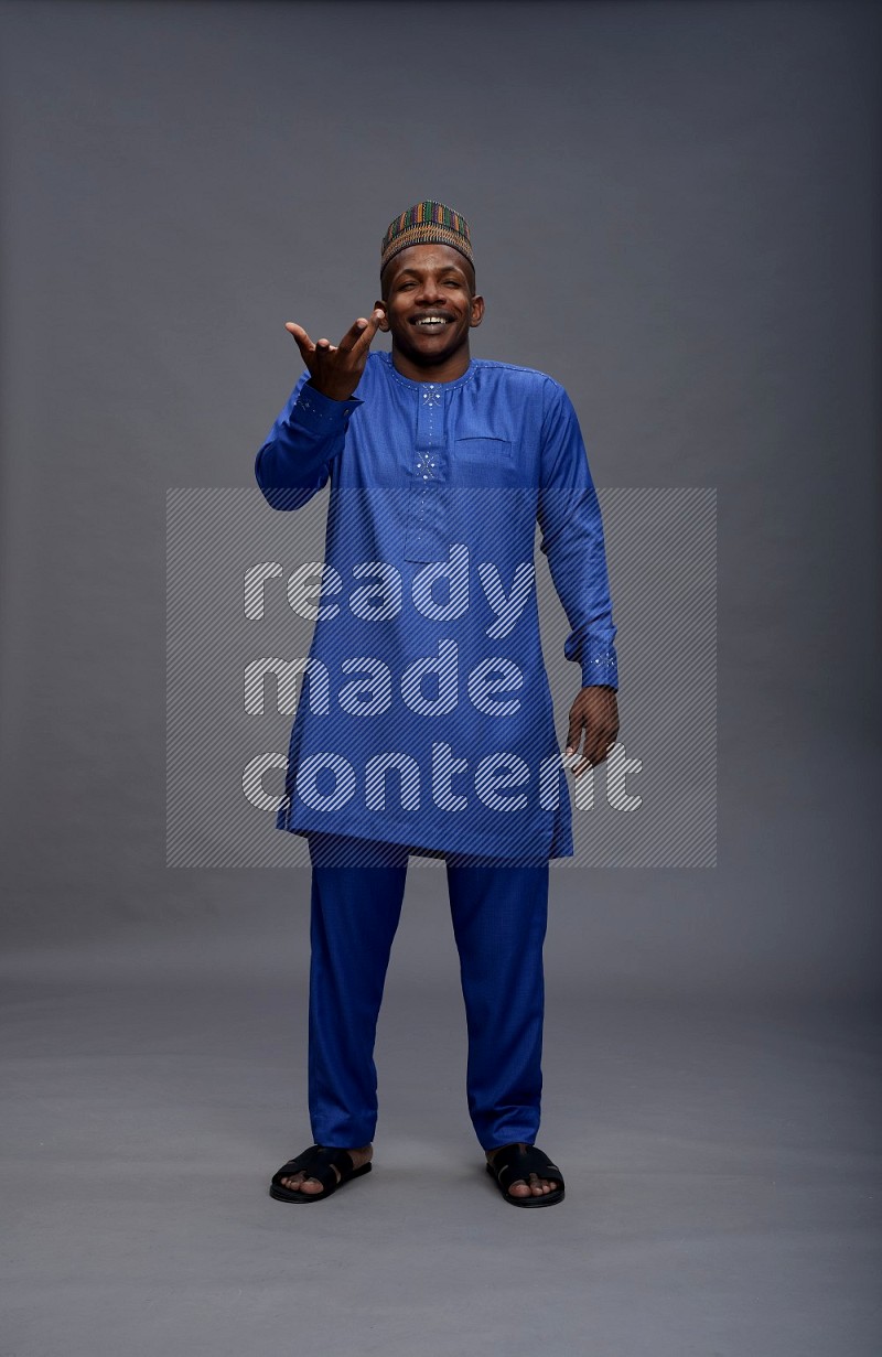 Man wearing Nigerian outfit standing interacting with the camera on gray background