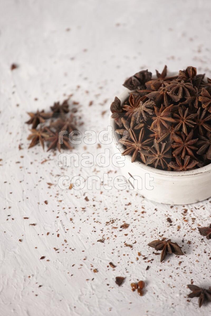 Star Anise in a white bowl and more of it sprinkled on white background