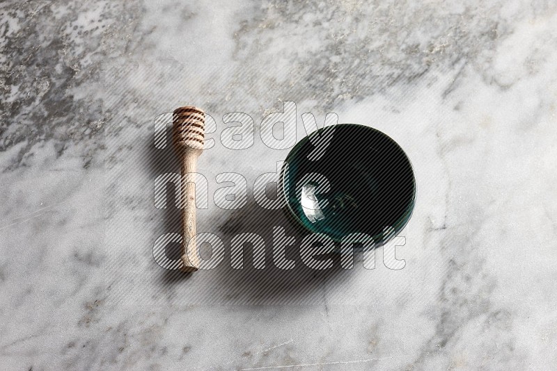 Dark Green Pottery bowl with wooden honey handle on the side with grey marble flooring, 65 degree angle