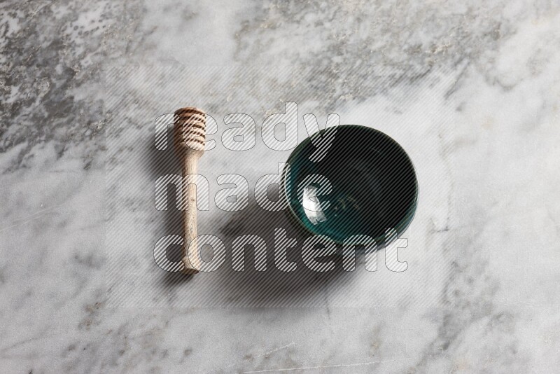 Dark green pottery bowl with wooden honey dipper on the side on grey marble background