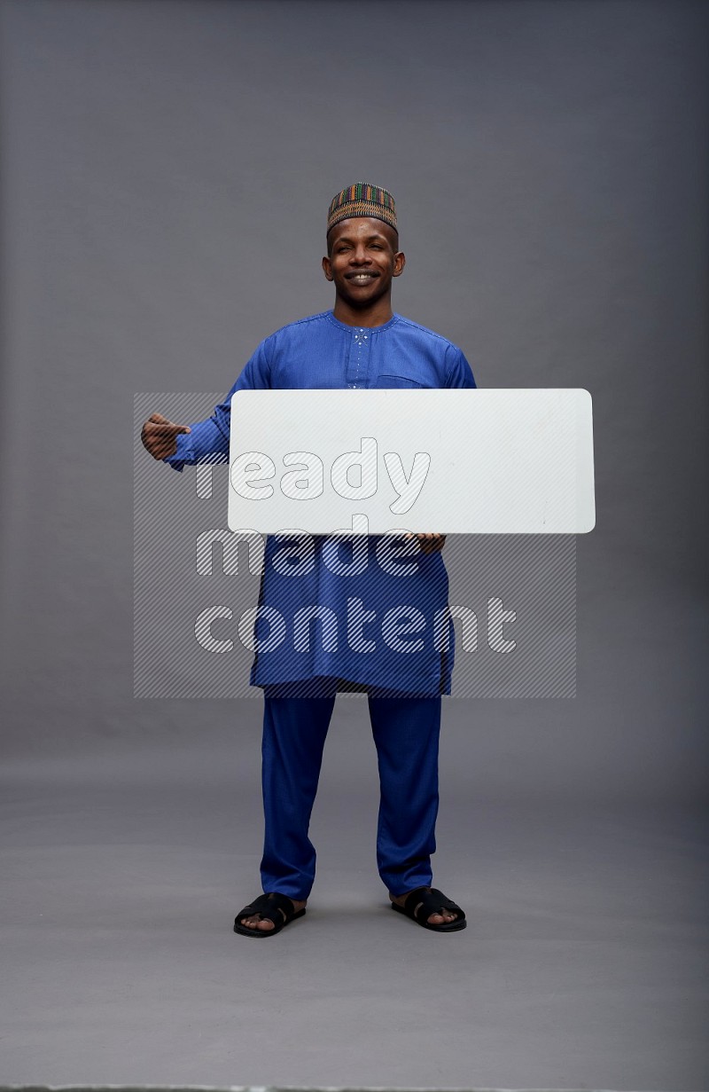 Man wearing Nigerian outfit standing holding board on gray background