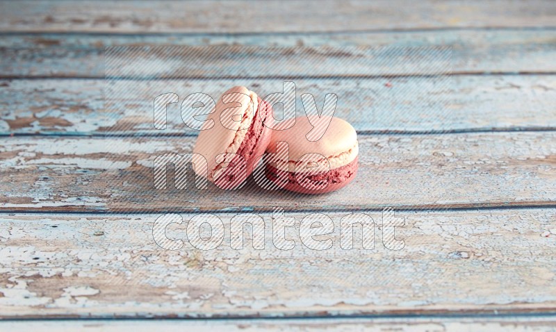 45º Shot of two Pink Litchi Raspberry macarons on light blue wooden background