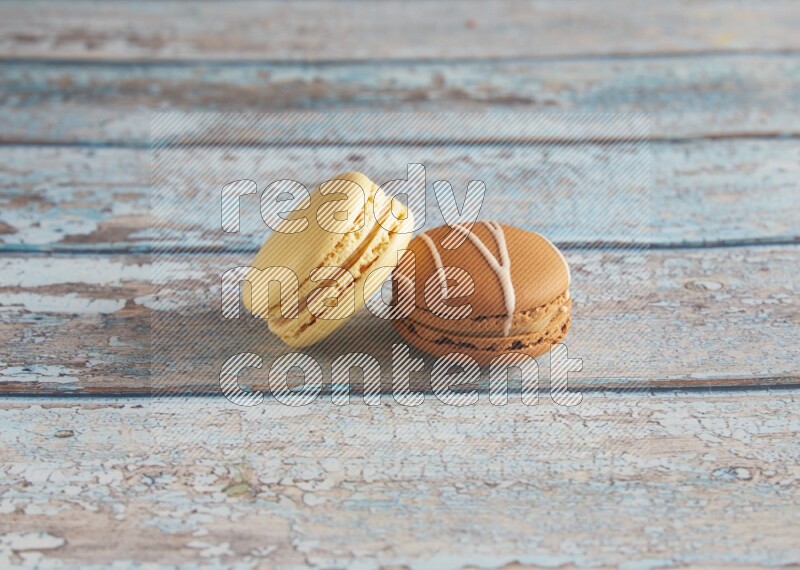 45º Shot of of two assorted Brown Irish Cream, and Yellow Vanilla macarons on light blue background