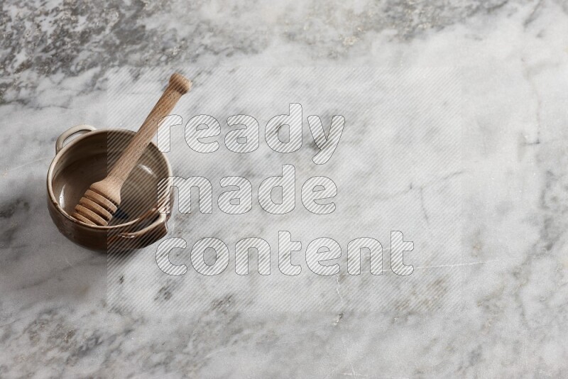 Multicolored pottery bowl with wooden honey dipper in it on grey marble background