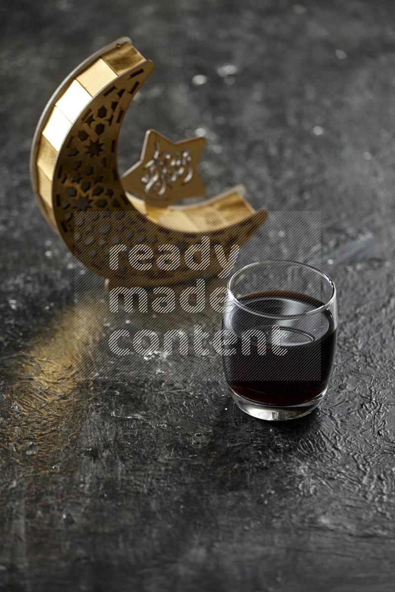 A crescent lantern with drinks, dates, nuts, prayer beads and quran on textured black background