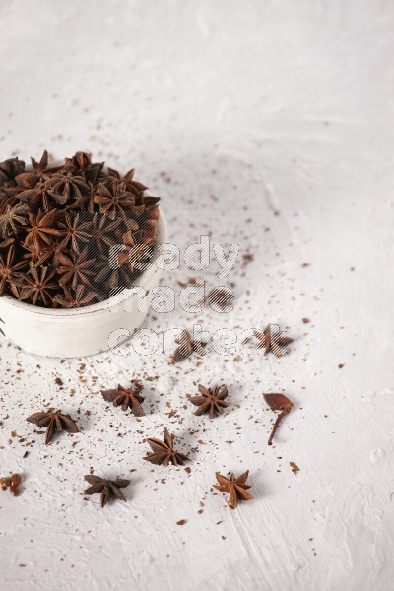 Star Anise in a white bowl and more of it sprinkled on white background