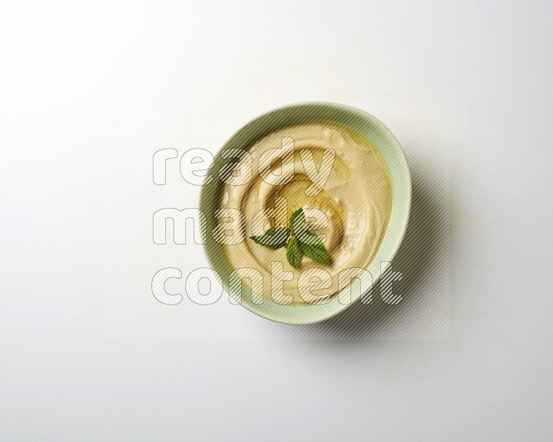 Hummus in a green plate garnished with mint on a white background