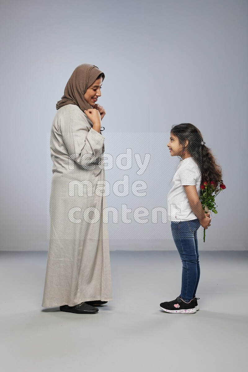 A girl standing giving flowers to her mother on gray background