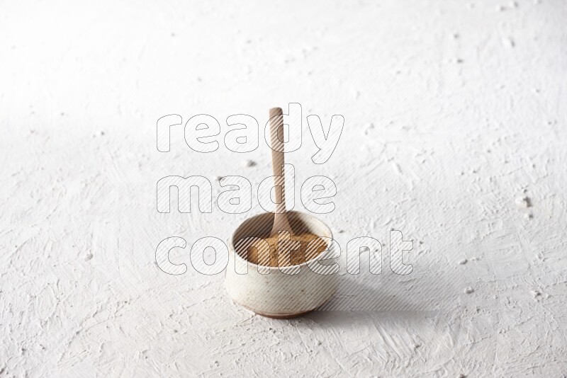 Ceramic beige bowl full of cinnamon powder with a wooden spoon on a textured white background