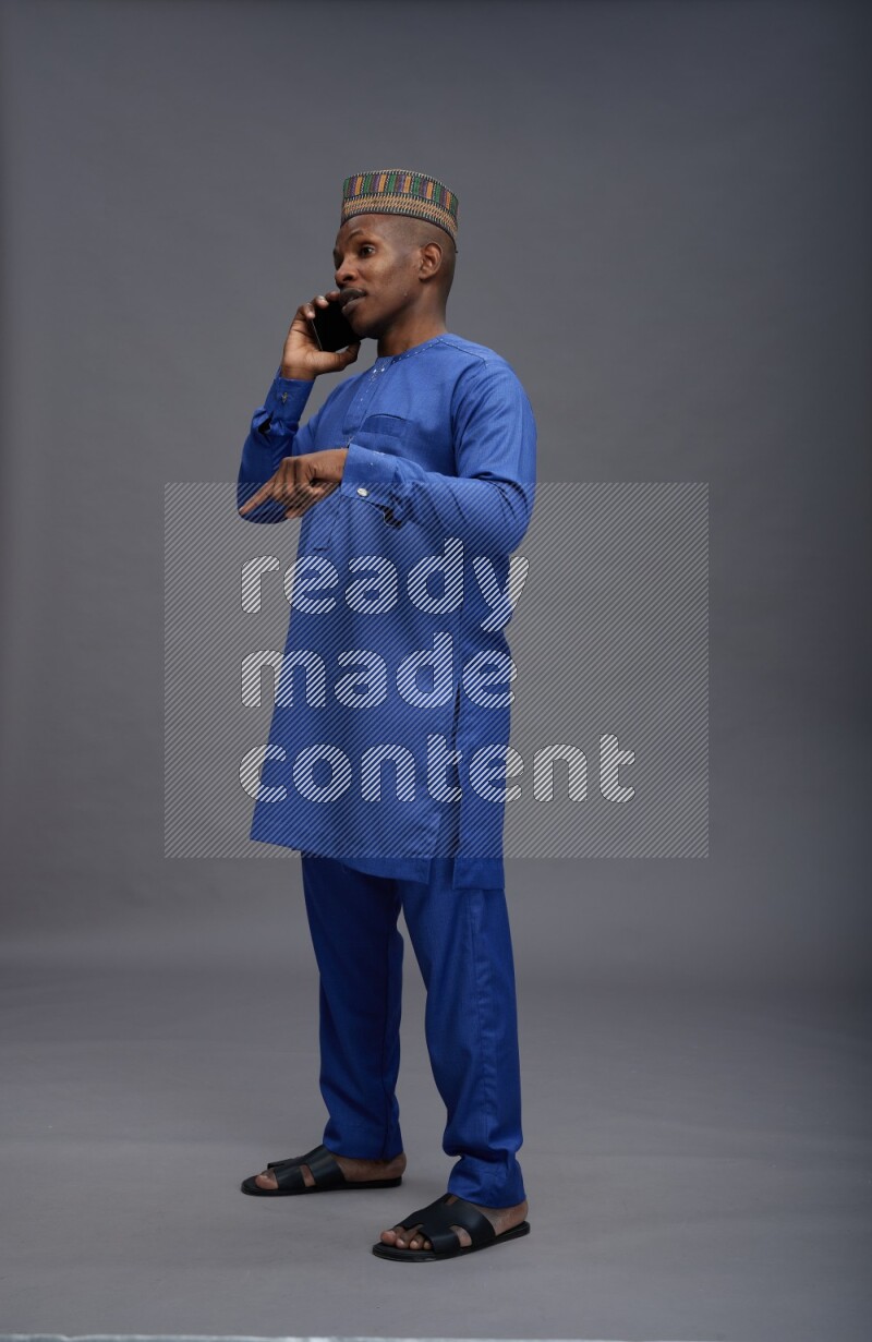 Man wearing Nigerian outfit standing talking on phone on gray background