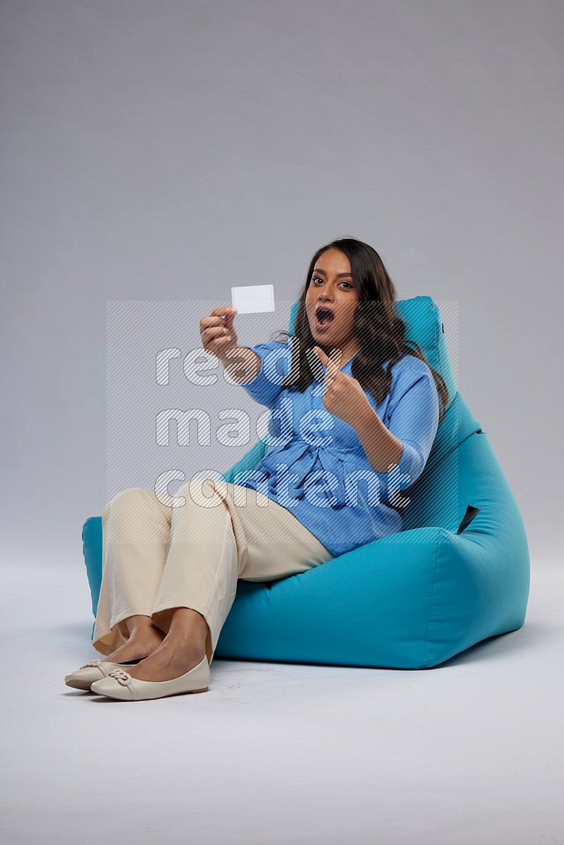 A woman sitting on a blue beanbag and holding ATM card