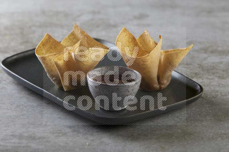 wonton cups with soy sauce ramkin on rectangle dark grey ceramic plate on grey textured counter top