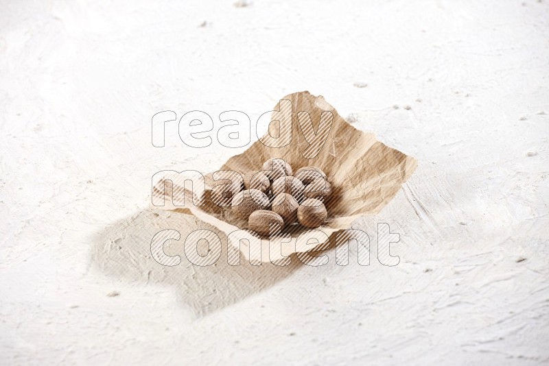 A crumpled piece of paper full of whole nutmeg seeds on a textured white flooring
