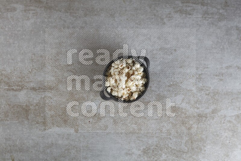 popcorn in a black handheld ceramic bowl on a grey textured countertop