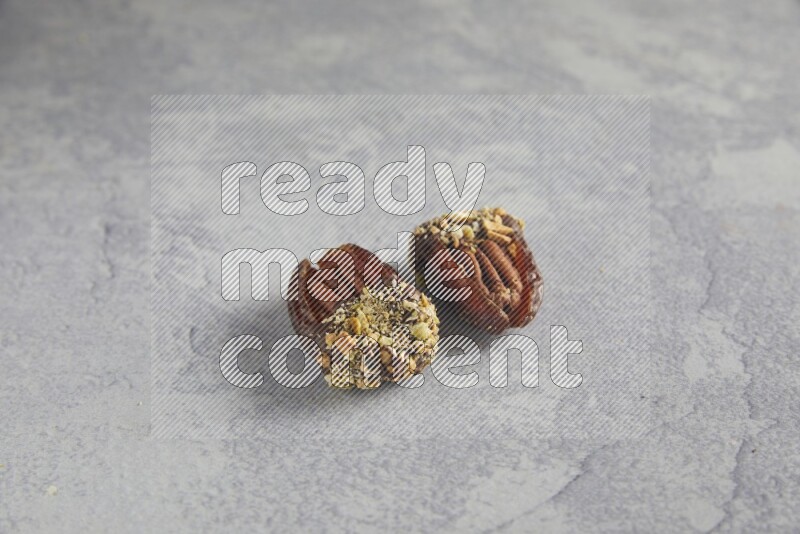 Two pecan stuffed dates covered with Dark chocolate and chopped pistachios on alight grey background