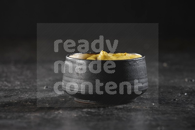 A black pottery bowl full of mustard paste on textured black flooring
