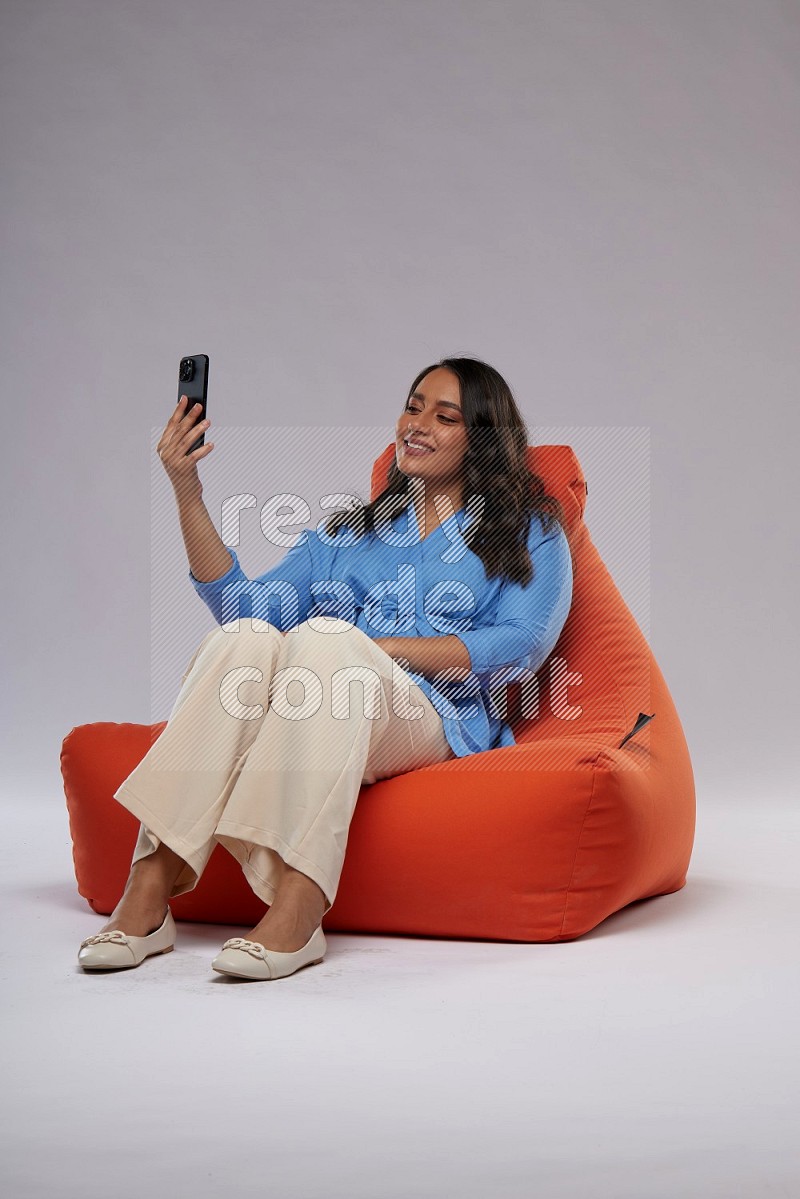 A woman sitting on an orange beanbag and taking selfie