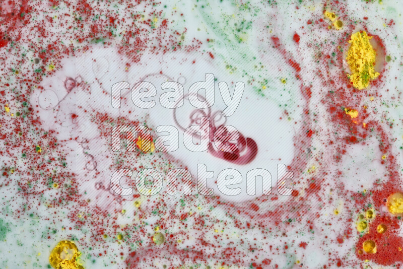 The image captures a splatter of yellow, red and green paint over a white backdrop