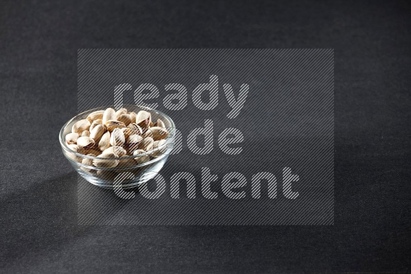 A glass bowl full of pistachios on a black background in different angles