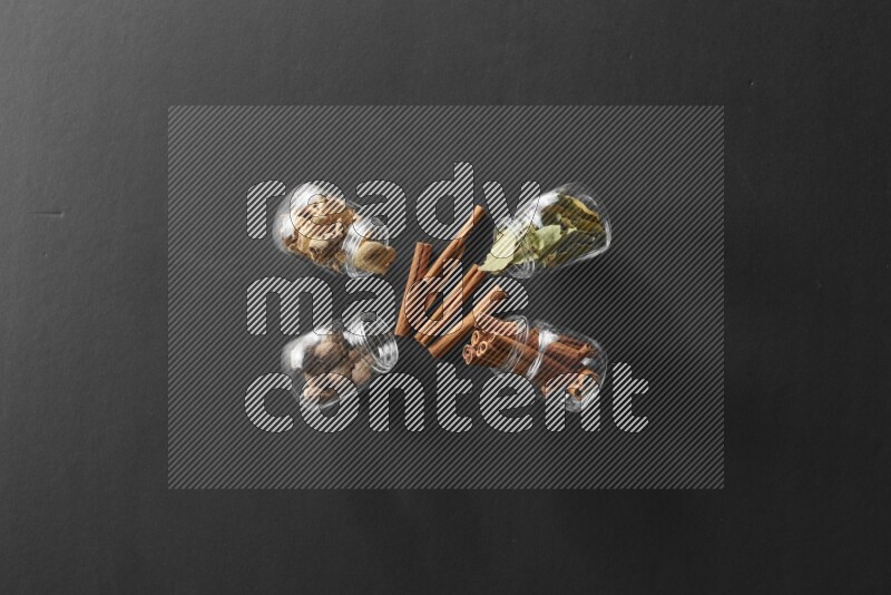 أوراق الغار وزنجبيل مجفف وقرفة وجوزة الطيب في أوعية زجاجية علي خلفية سوداء