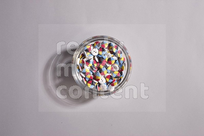 A glass bowl full of colored buttons on grey background