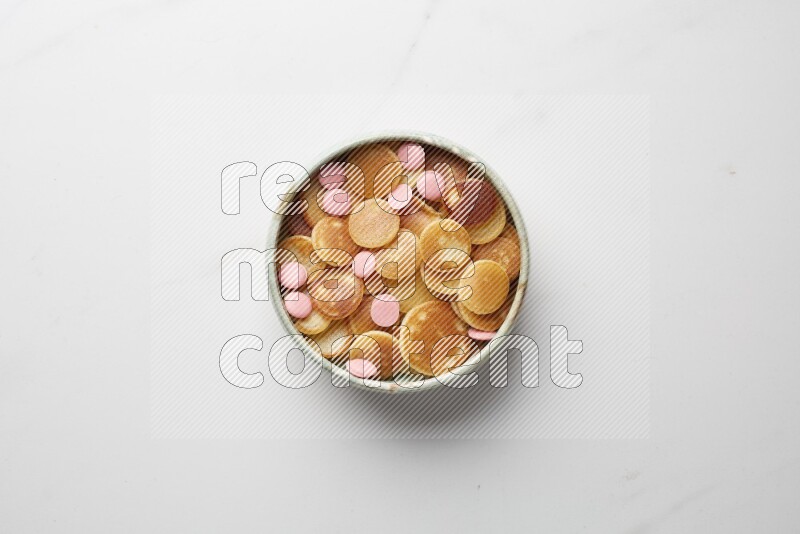 Top-view shot of pink chocolate chips cereal pancakes in a round bowl on white background