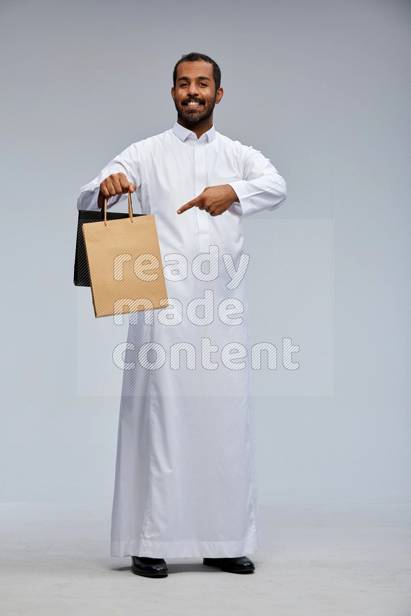 Saudi man Wearing thob standing holding shopping bag on Gray background