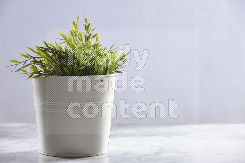 Green artificial plant in white pot on grey marble background
