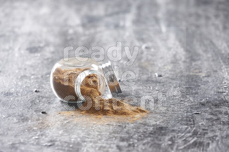 Flipped herbal glass jar full of cinnamon powder on textured black background
