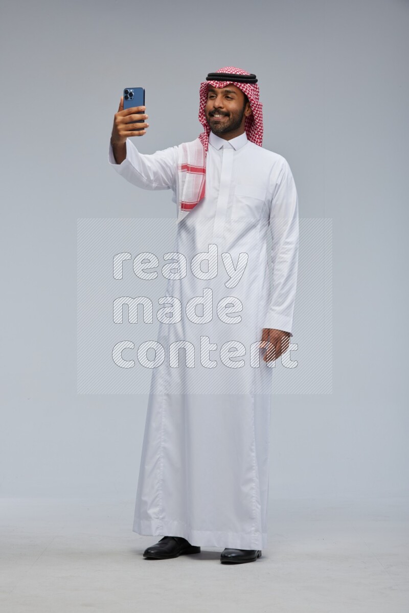 Saudi man Wearing Thob and shomag standing taking selfie on Gray background