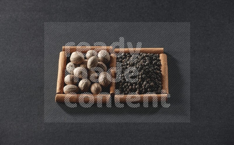 مربعان من أعواد القرفة ممتلئان بجوزة الطيب وحبوب الفلفل الأسود علي خلفية سوداء