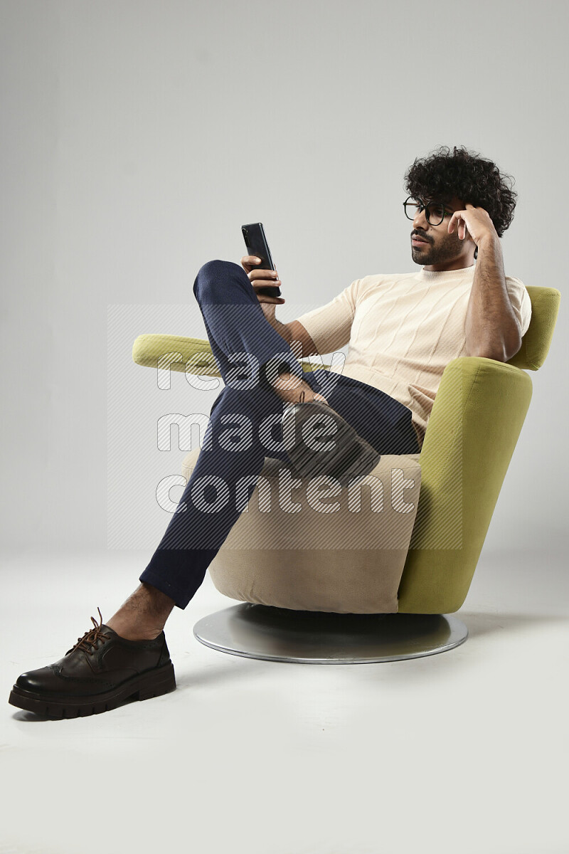 رجل يرتدي ملابس كاجوال يجلس علي كرسي و يرسل رسائل نصية علي الهاتف علي خلفية بيضاء