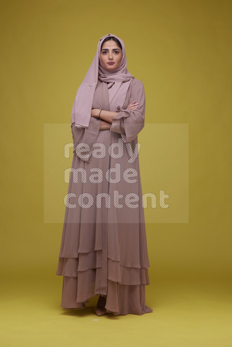 A woman Posing on a Yellow Background wearing Brown Abaya with Hijab