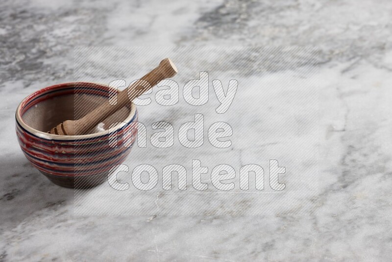 Multicolored pottery bowl with wooden honey dipper in it on grey marble background