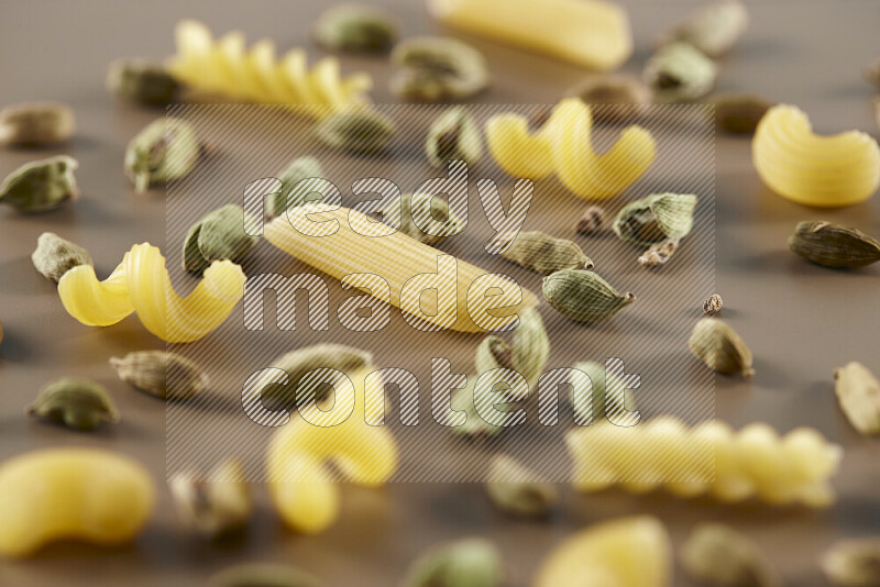 Raw pasta with different ingredients such as cherry tomatoes, garlic, onions, red chilis, black pepper, white pepper, bay laurel leaves, rosemary and cardamom on beige background