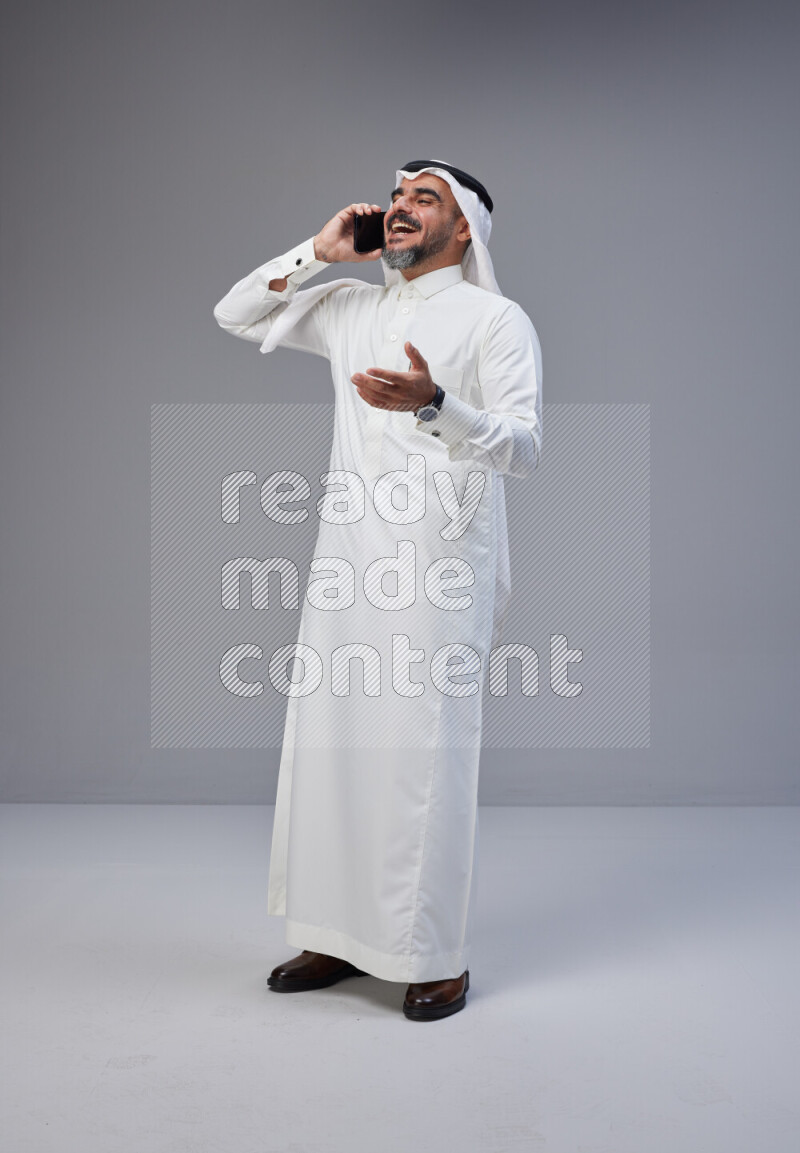 Saudi man Wearing Thob and white Shomag standing talking on phone on Gray background
