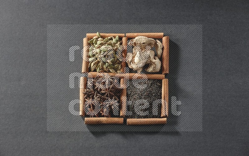 4 مربعات من عيدان القرفة ممتلئة بالشاي واليانسون النجمي والزنجبيل المجفف وحب الهيل على أرضية سوداء