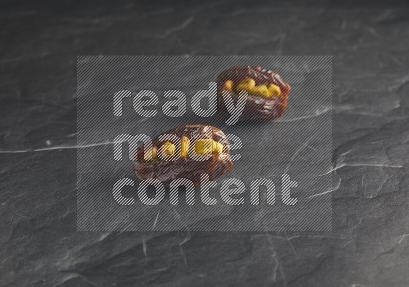 two pistachios stuffed madjoul dates on a black textured background