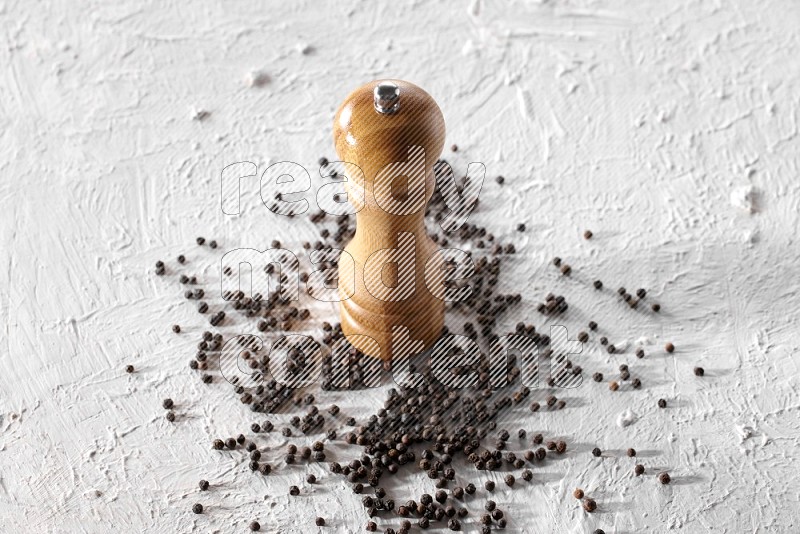 A wooden grinder with black pepper beads on a textured white flooring