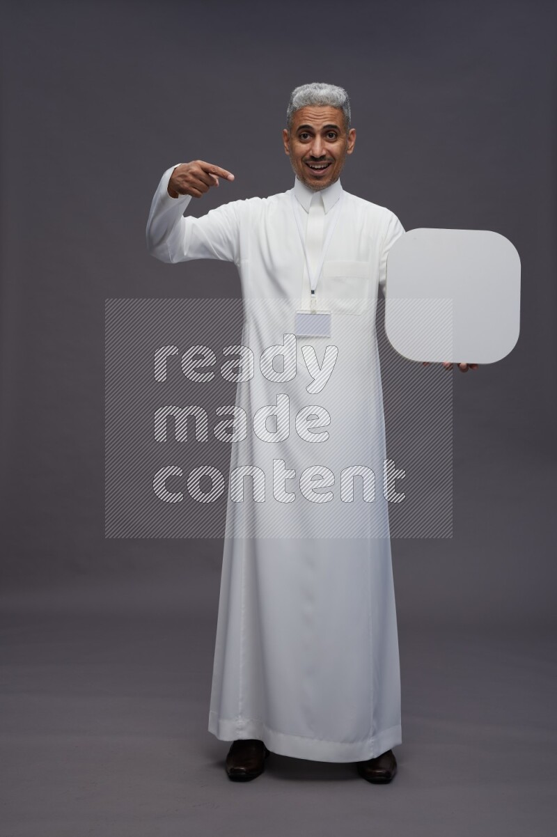 Saudi man wearing thob with neck strap employee badge standing holding social media sign on gray background