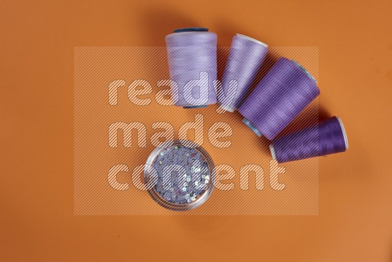 A purple collection of sewing and tailoring tools arranged on a orange background