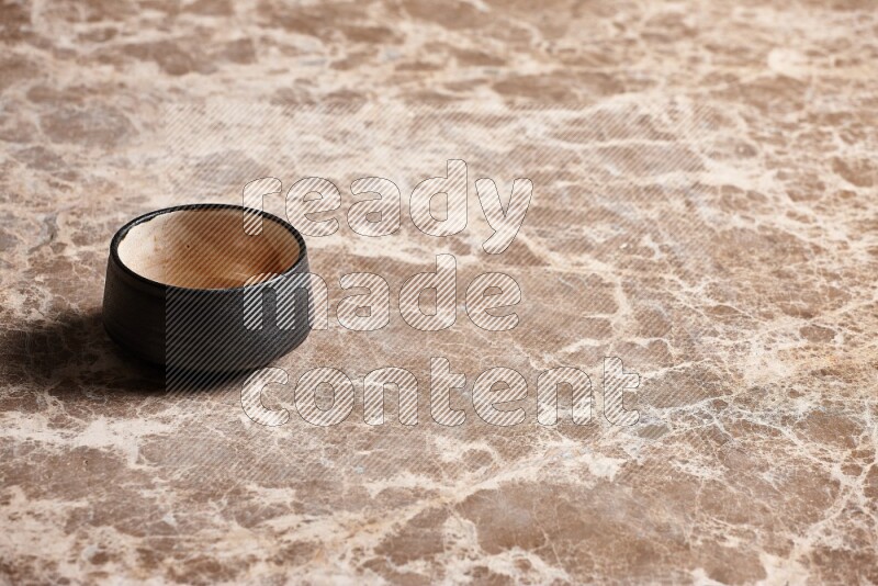 A black pottery bowl on beige marble background